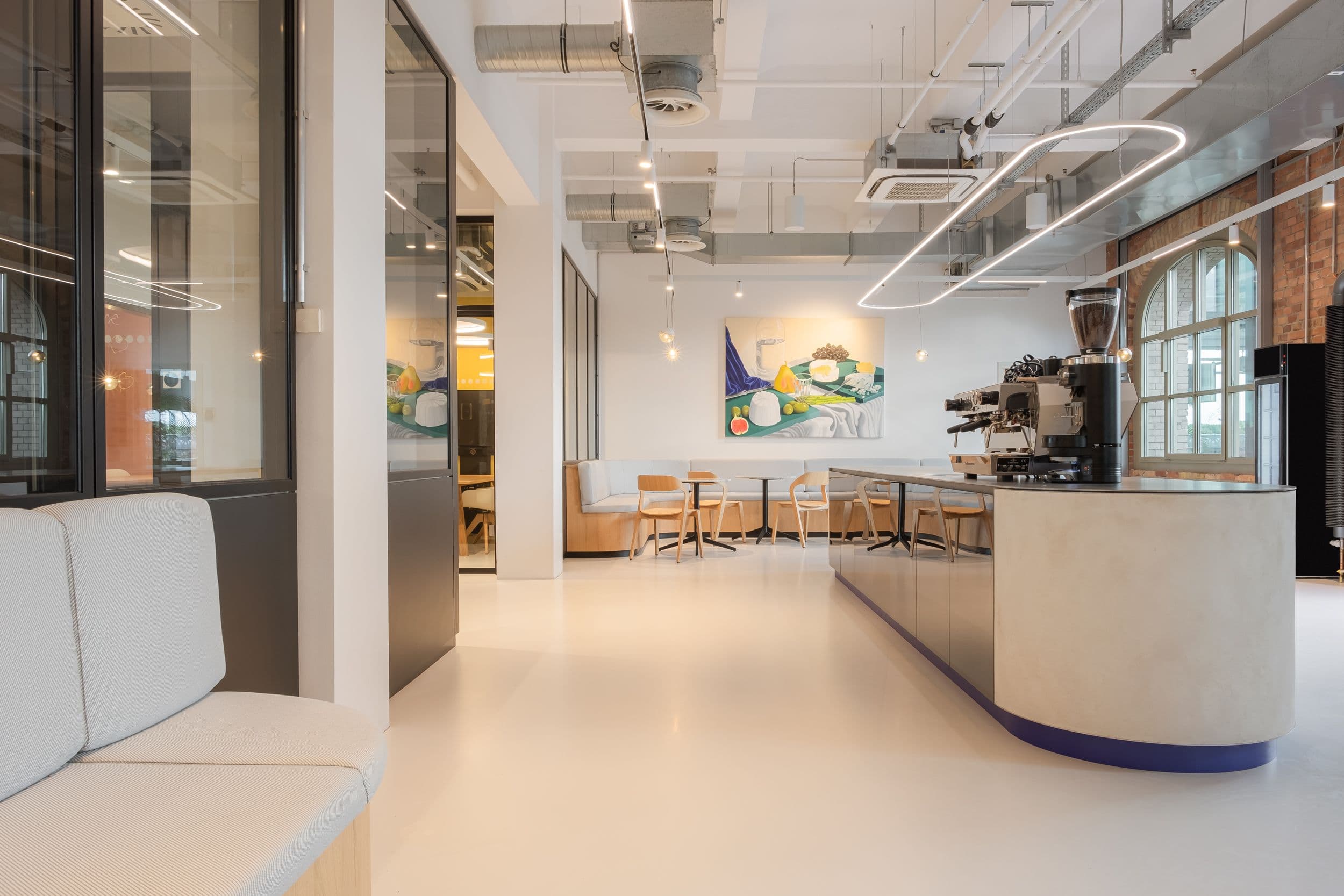 Empfangsbereich der Formo Zentrale Berlin mit geschwungener Rezeptionstheke, großformatigem Käse-Stillleben-Gemälde, Kaffeebar und Sitzlounge in hellem Industrial-Loft mit Backsteinwänden, Innenarchitektur Susanne Philippson