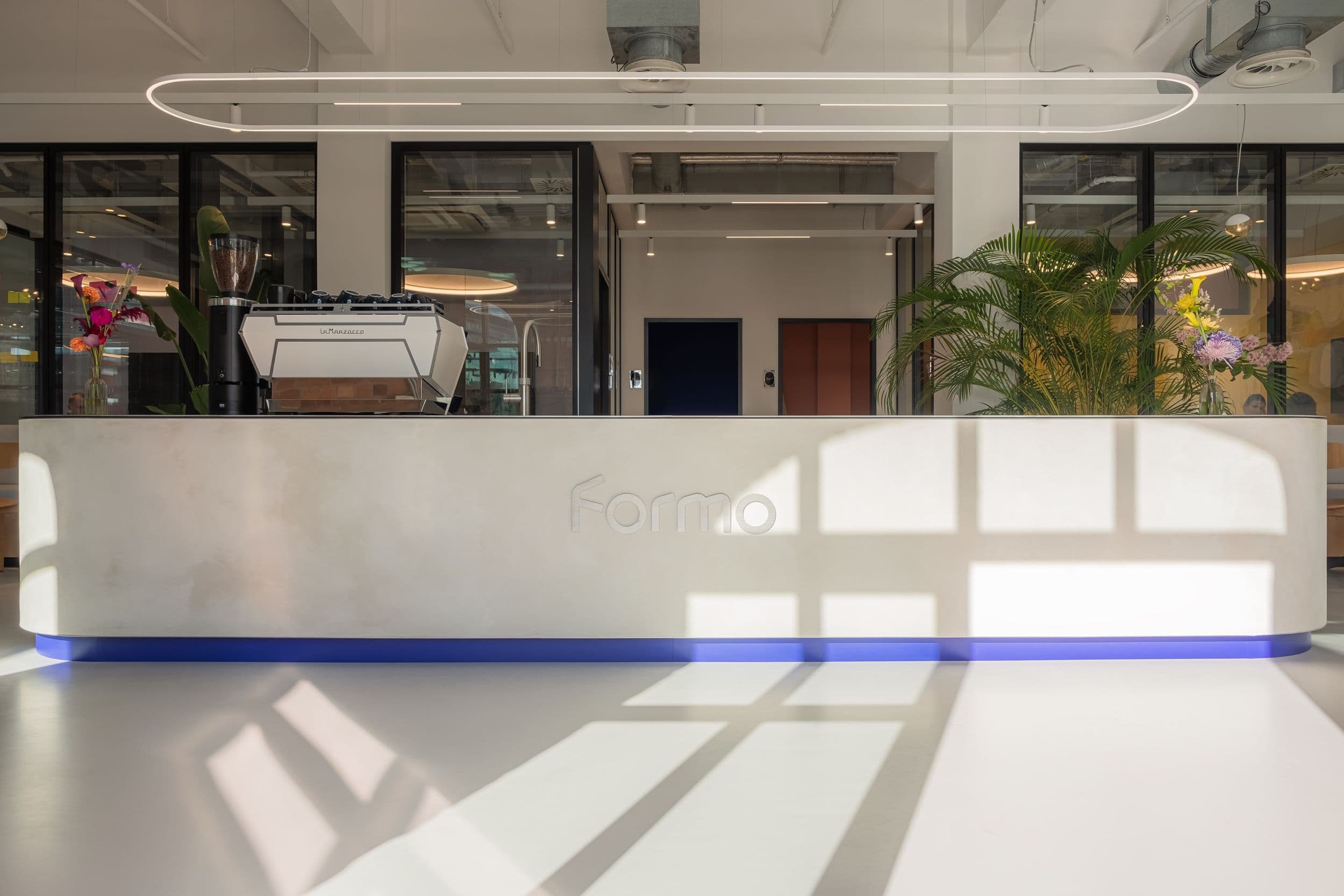 Empfangsbereich der Formo Zentrale Berlin mit geschwungener Rezeptionstheke, großformatigem Käse-Stillleben-Gemälde, Kaffeebar und Sitzlounge in hellem Industrial-Loft mit Backsteinwänden, Innenarchitektur Susanne Philippson