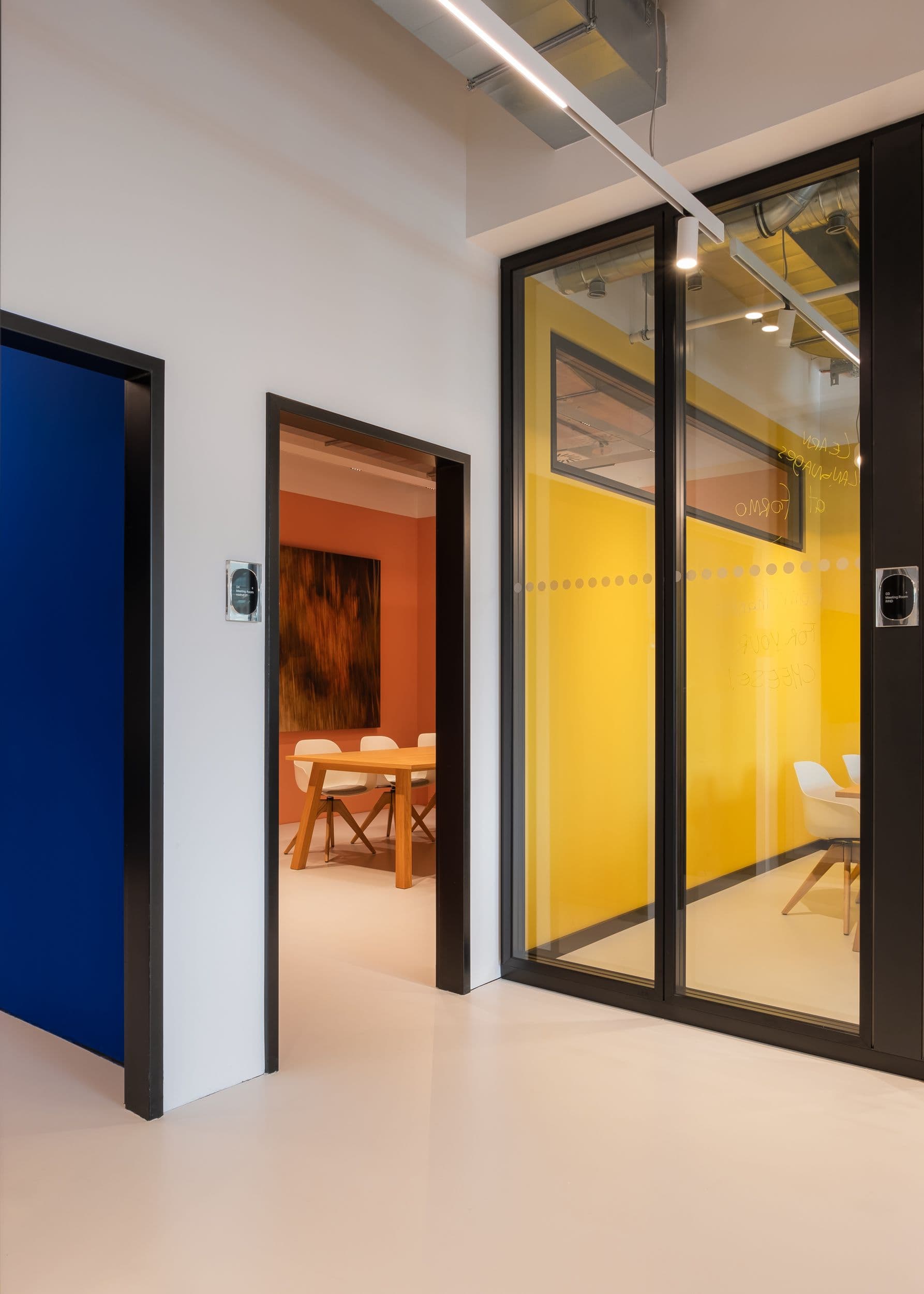 Farbige Besprechungsräume der Formo Zentrale Berlin mit gelber und terrakottafarbener Wandgestaltung, Eichentischen, weißen Schalenstühlen und Glastrennwänden mit Beschriftung, Innenarchitektur Susanne Philippson