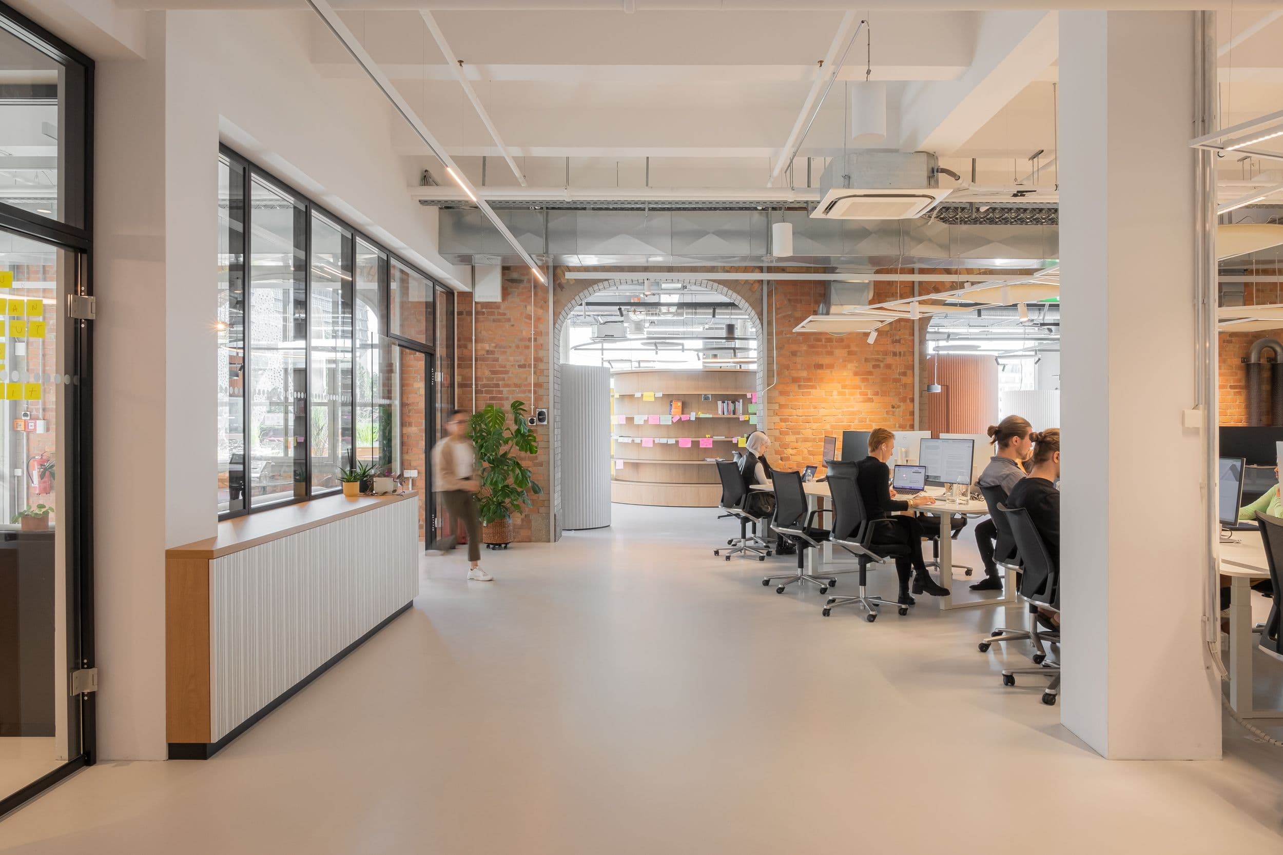 Offener Arbeitsbereich der Formo Zentrale Berlin mit Backsteinbögen, höhenverstellbaren Schreibtischen, quadratischen Akustik-Lichtdecken und Blick auf den zentralen Kollaborationsbereich, Innenarchitektur Susanne Philippson