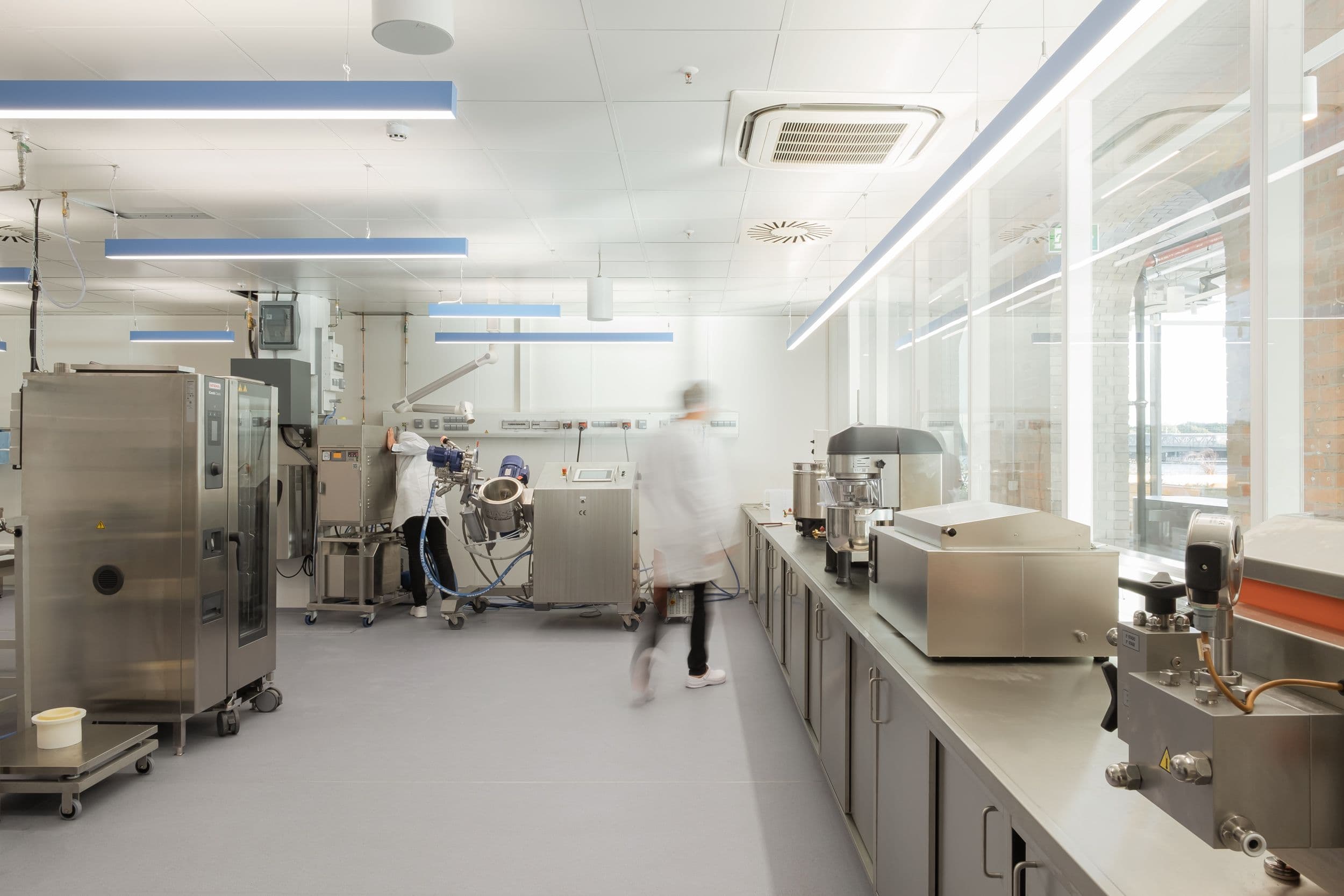 Forschungslabor und Pilotproduktion der Formo Zentrale Berlin mit Edelstahlgeräten, weißen Laborarbeitstischen und Regalwänden in hellem Industrial-Loft mit Backsteinbögen, Innenarchitektur Susanne Philippson