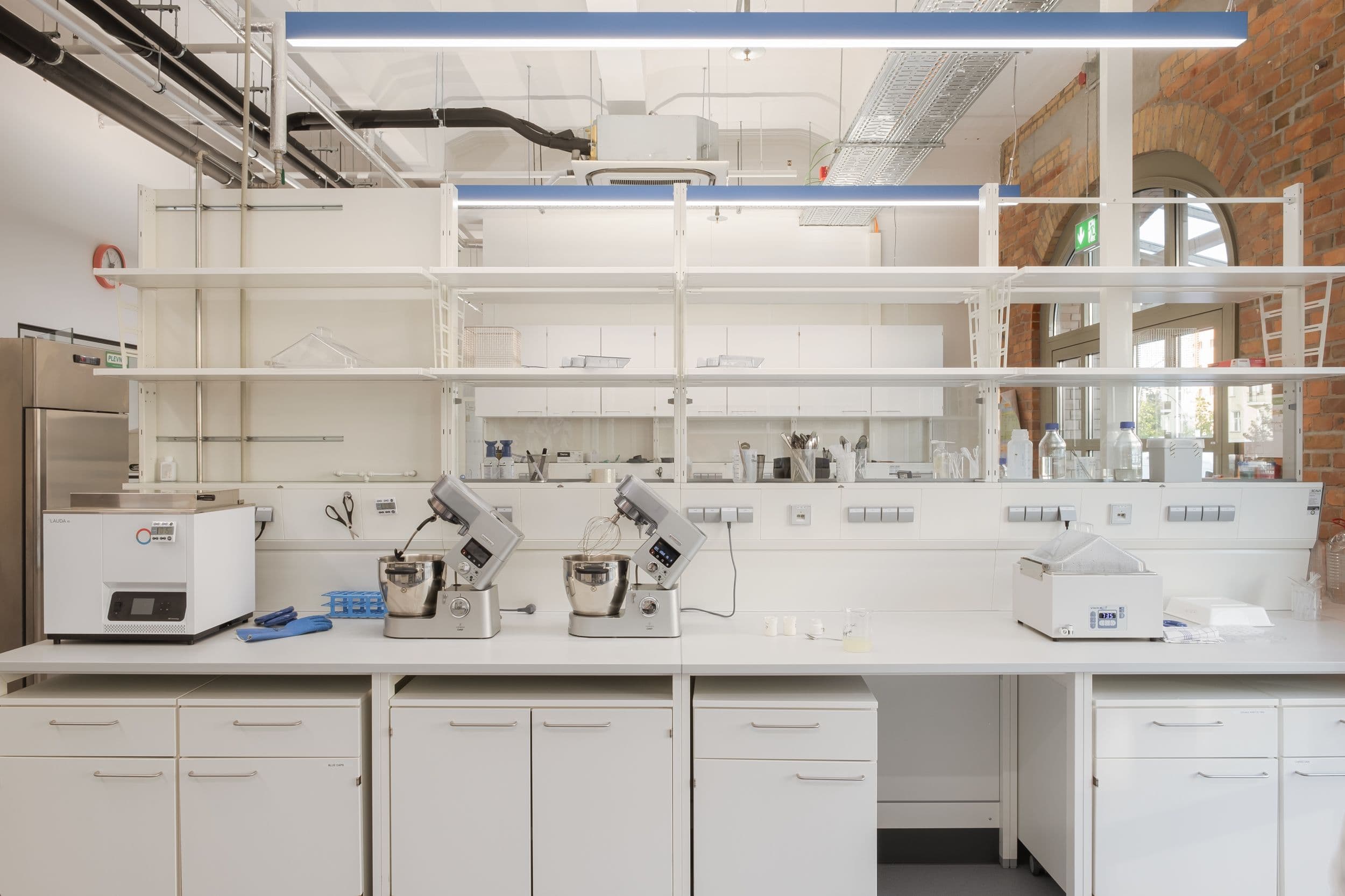 Forschungslabor und Pilotproduktion der Formo Zentrale Berlin mit Edelstahlgeräten, weißen Laborarbeitstischen und Regalwänden in hellem Industrial-Loft mit Backsteinbögen, Innenarchitektur Susanne Philippson