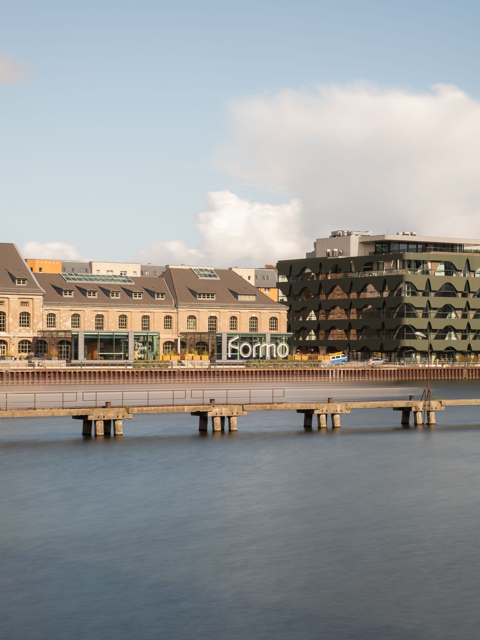 Blick auf das Formo Gebäude am Berliner Spreeufer mit Molecule Man Skulptur sowie großformatige Glasfassadenbeschriftung mit Markenbotschaft und versilberter Kuh-Skulptur im Eingangsbereich, Innenarchitektur Susanne Philippson
