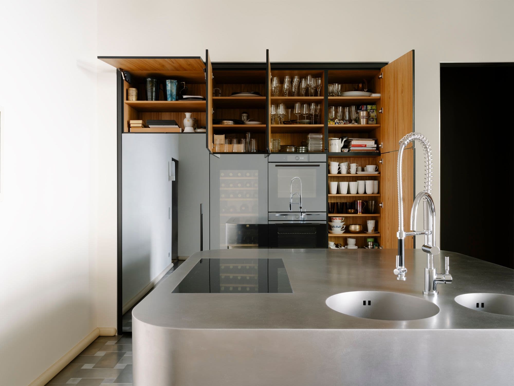 Maßgefertigte Einbauküche in einer Berliner Altbauwohnung mit geschwungener Edelstahlinsel, verspiegelter Schrankwand, Weinkühlschrank und geöffneten Holzinnenschränken, Innenarchitektur Susanne Philippson