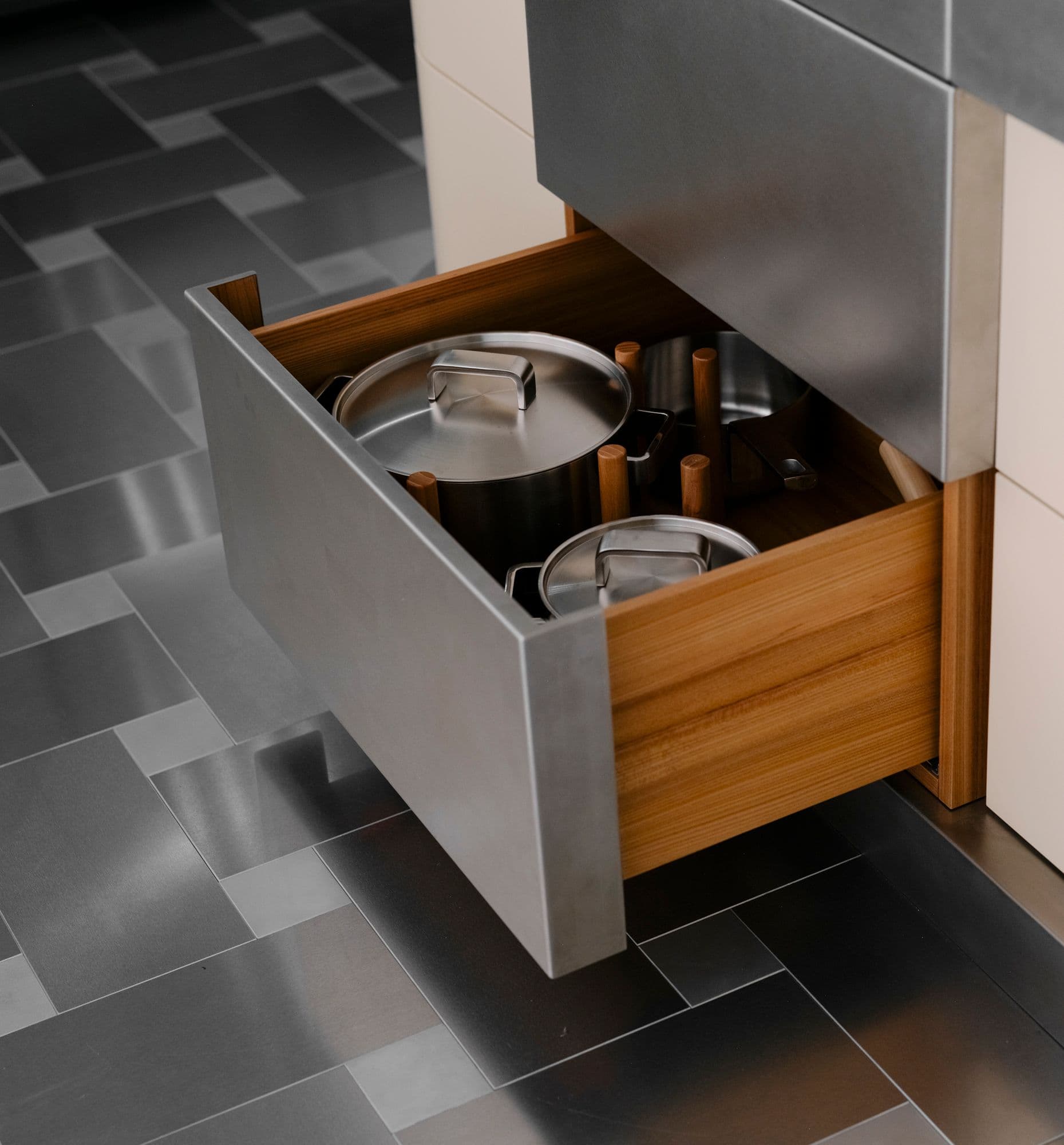 Maßgefertigte Edelstahlkücheninsel einer Berliner Altbauwohnung mit geöffneter Schublade mit Holzeinsatz, zweifarbigem Fliesenboden im Schachbrettmuster und geschlossener sowie geöffneter Spülmaschine, Innenarchitektur Susanne Philippson