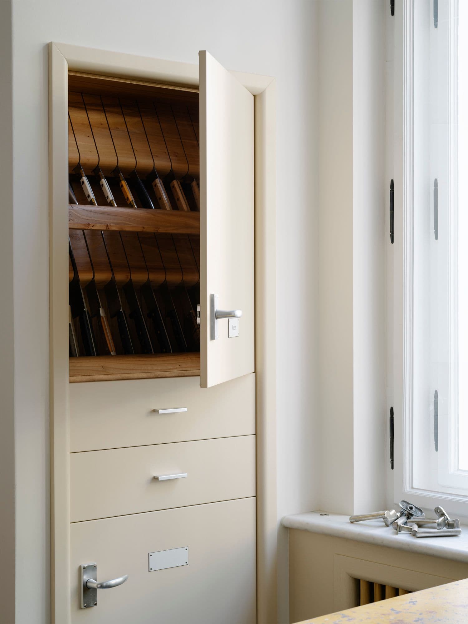 Maßgefertigter Einbauschrank in einer Berliner Altbauwohnung mit geöffnetem Holzeinsatz für Messeraufbewahrung, Schubladen und zweifarbigem Fliesenboden im Schachbrettmuster, Innenarchitektur Susanne Philippson