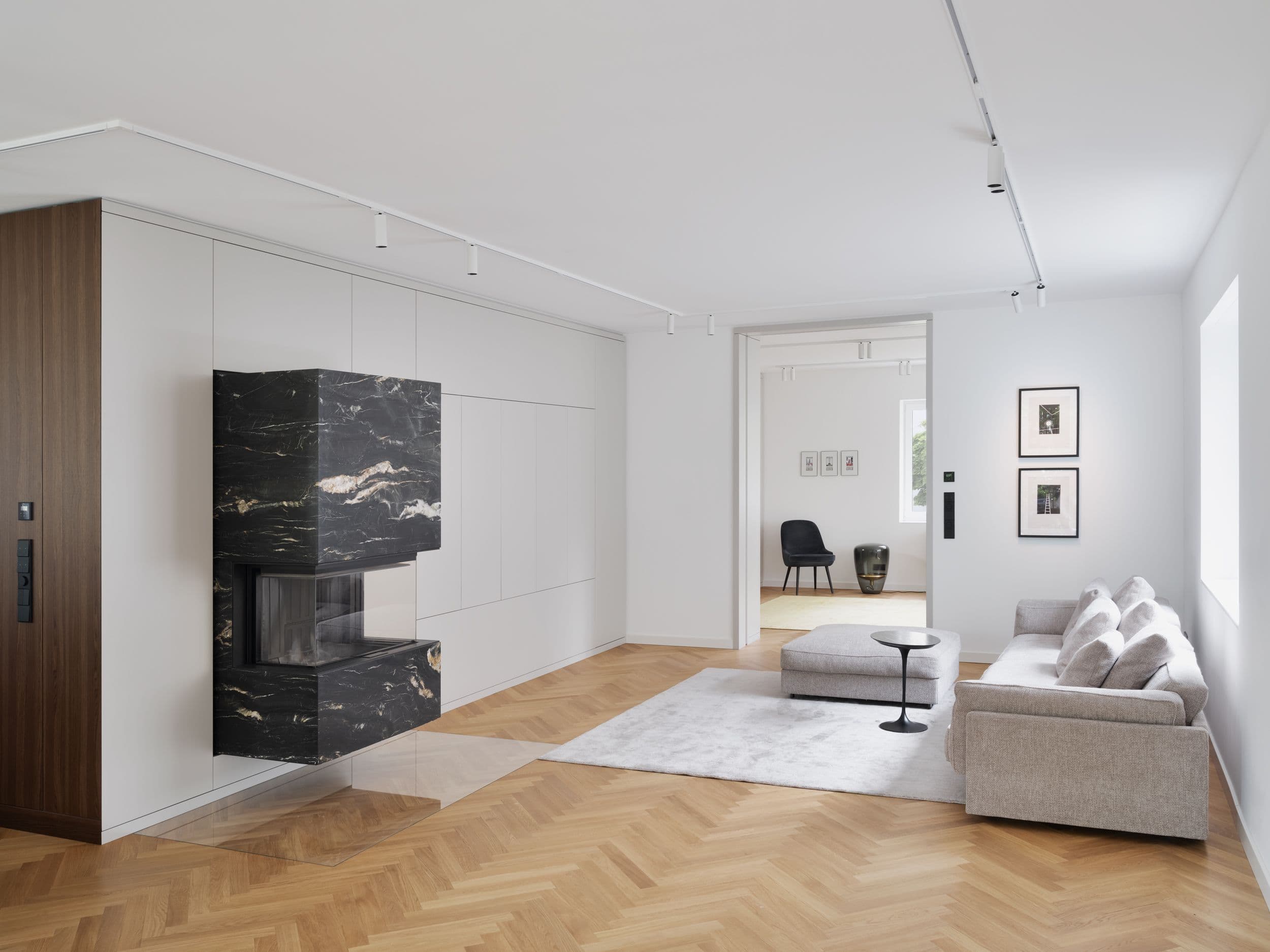 Wohnzimmer mit schwarzem Marmorkamin in maßgefertigter Einbauwand, Fischgrätparkett und reduzierter Möblierung, Innenarchitektur Susanne Philippson