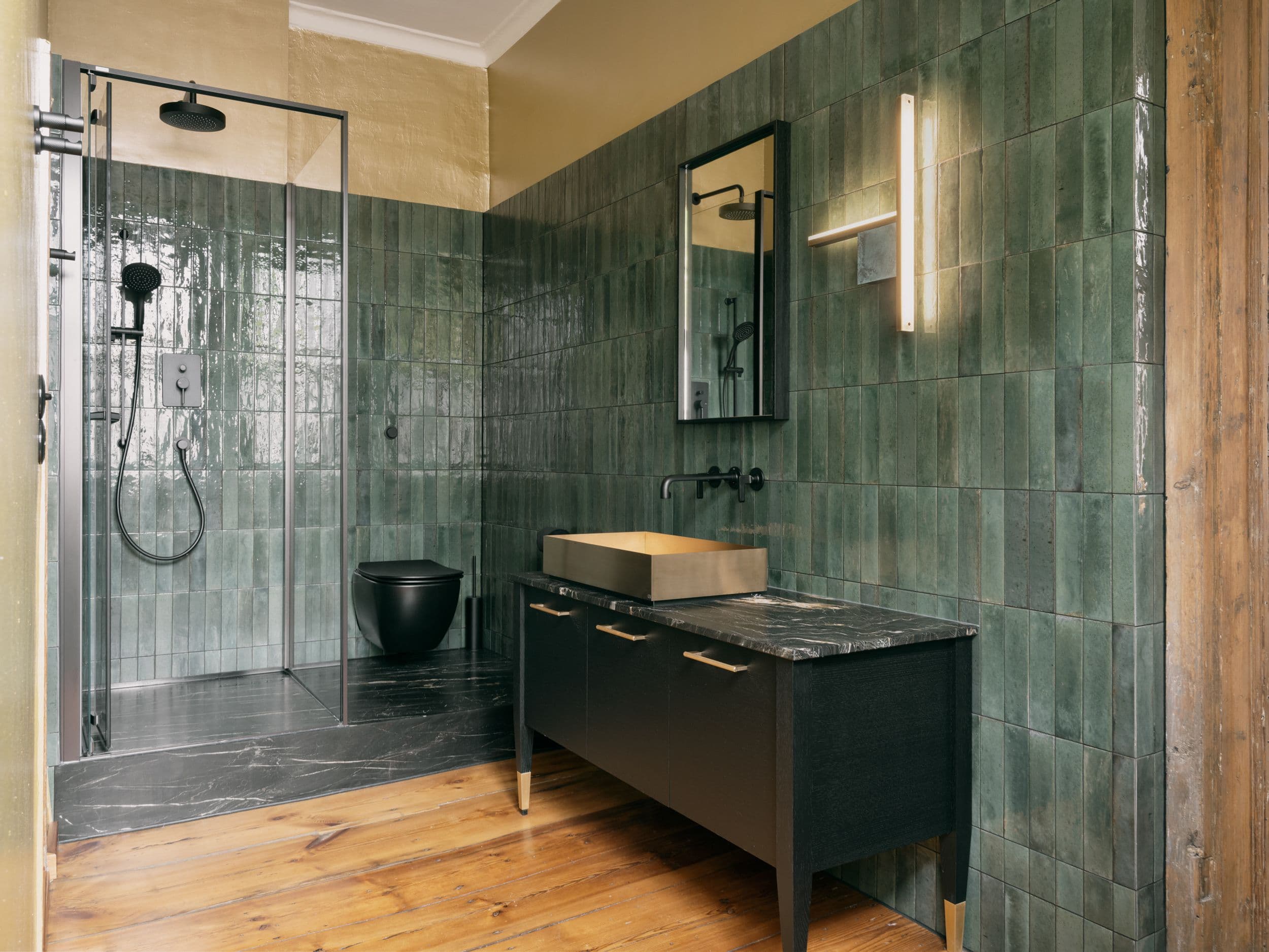 Badezimmer der B21 in Potsdam mit grünen Zellige-Wandfliesen, Regendusche, schwarzem Sanitär und dunklem Waschtisch mit Marmorplatte auf historischen Kieferndielen, Innenarchitektur Susanne Philippson