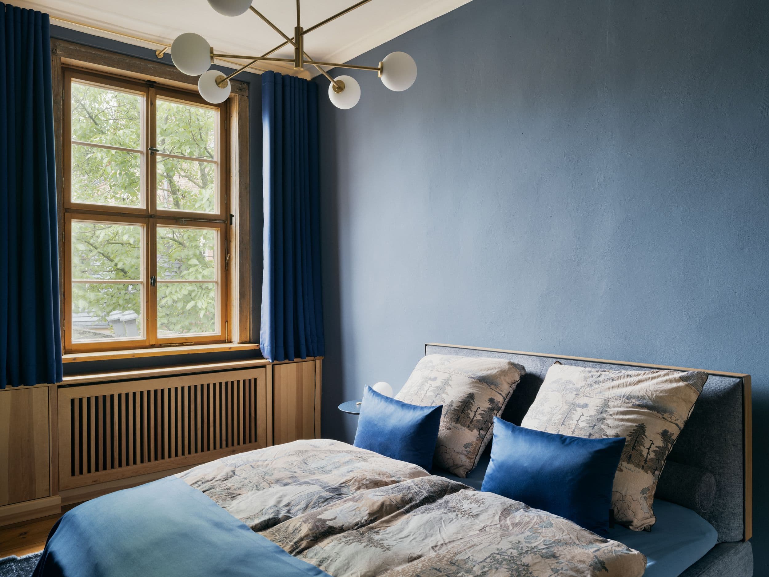 Schlafzimmer der B21 in Potsdam mit taubenblauer Wandgestaltung, Doppelbett, Messingpendelleuchte und maßgefertigter Holzverkleidung am Heizkörper, Innenarchitektur Susanne Philippson