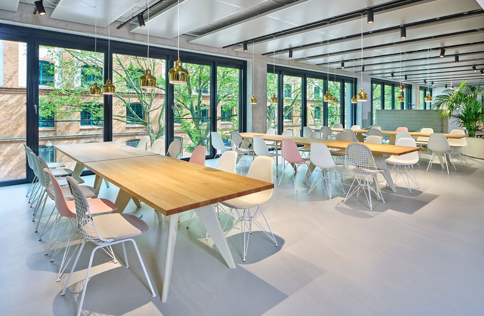 Heller Speise- und Gemeinschaftsbereich mit Eichentischen, Vitra-Stühlen und goldenen Pendelleuchten im Merantix Campus Berlin