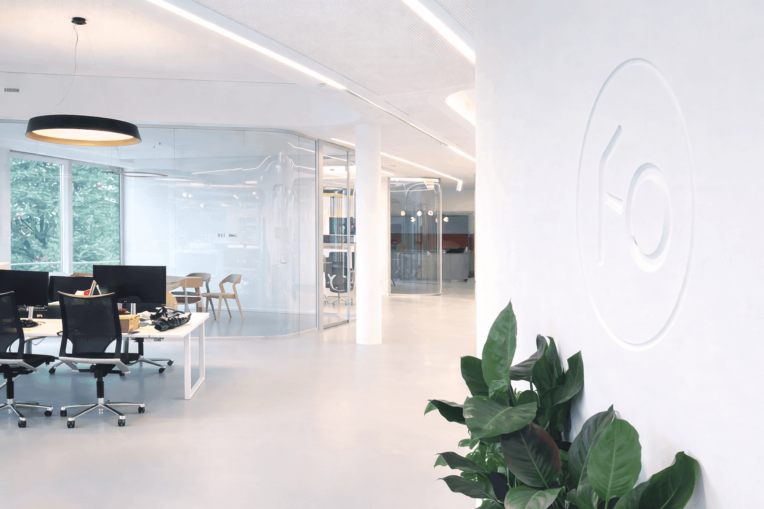 Offener Arbeitsbereich mit Arbeitsplätzen, geschwungener Glastrennwand, integrierter Deckenbeleuchtung und Relief-Logo an weißer Wand im Büro Formo Frankfurt, Innenarchitektur Susanne Philippson