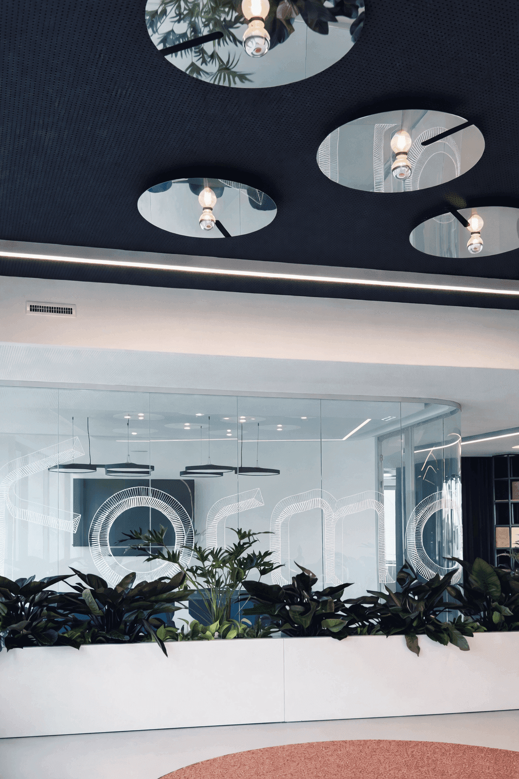 Empfangsbereich mit geschwungener Glastrennwand, Formo-Schriftzug auf Glas, eingelassenem Deckenspiegeln, Pflanztrögen und blauem Besprechungsraum mit markanten Sitzmöbeln im Büro Formo Frankfurt, Innenarchitektur Susanne Philippson