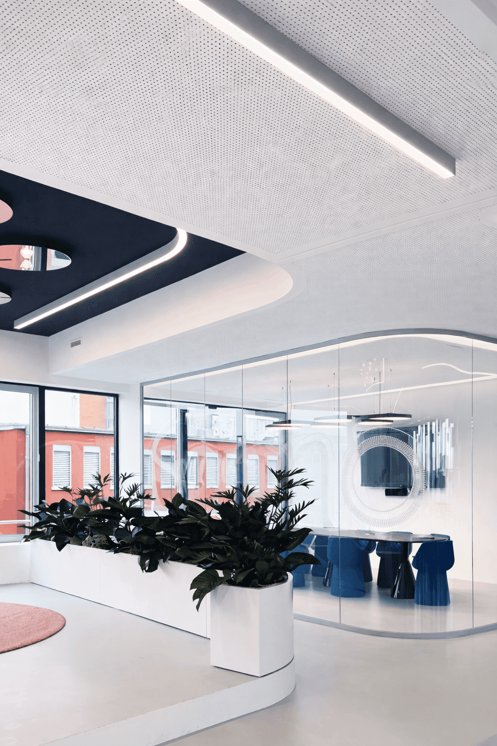 Empfangsbereich mit geschwungener Glastrennwand, Formo-Schriftzug auf Glas, eingelassenem Deckenspiegeln, Pflanztrögen und blauem Besprechungsraum mit markanten Sitzmöbeln im Büro Formo Frankfurt, Innenarchitektur Susanne Philippson