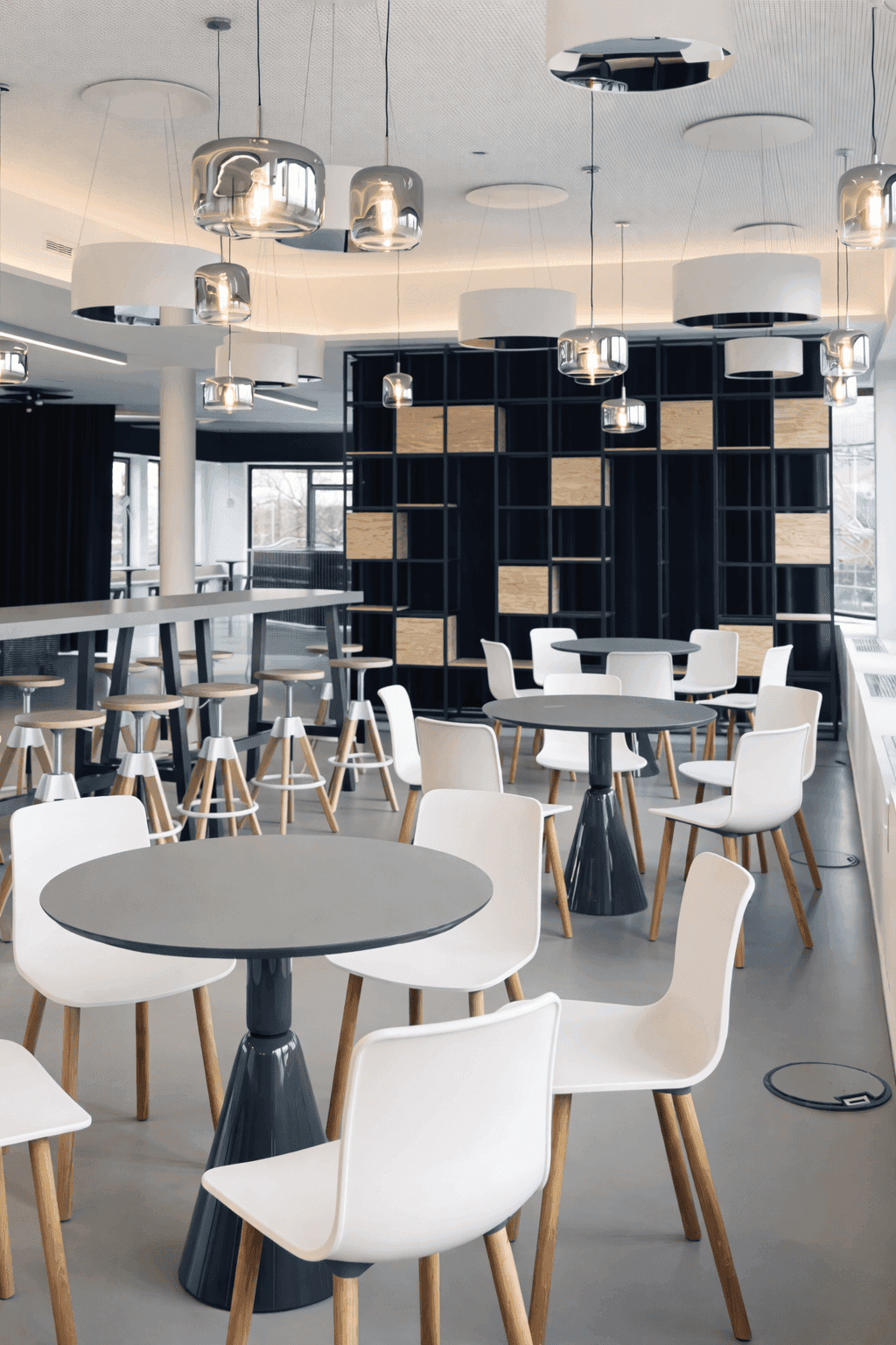 Kantine mit runden Tischen, weißen Wilkhahn-Stühlen mit Holzbeinen, Barhockern, rauchglasfarbenen Pendelleuchten und dunklem Regalraster mit Holzeinsätzen im Büro Formo Frankfurt, Innenarchitektur Susanne Philippson