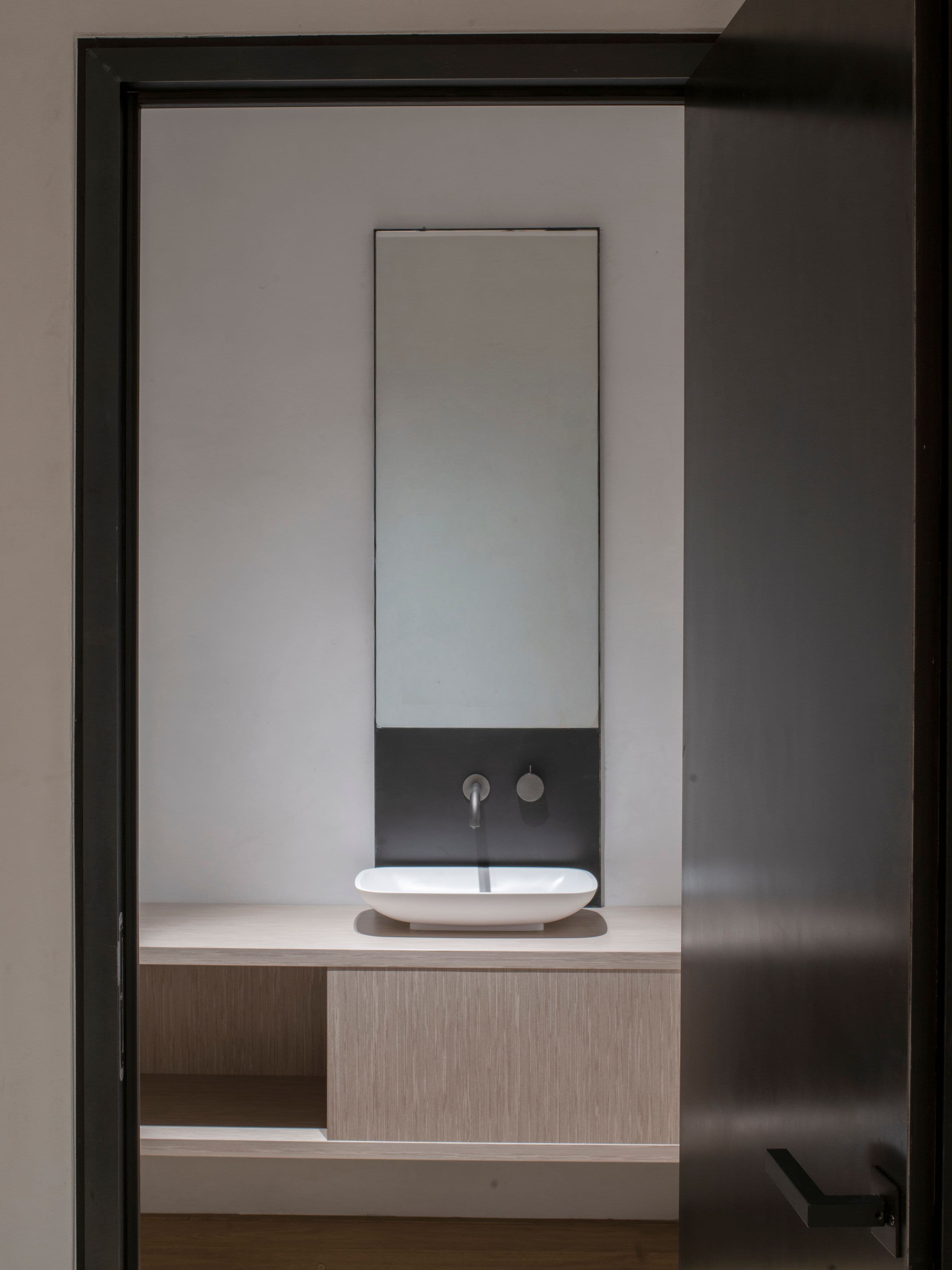 Gäste-WC mit aufgesetztem Aufsatzwaschbecken, schmalem Spiegel und Wandarmatur auf Schwarzstahlrückwand in einem Privathaus in Tirol, Innenarchitektur Susanne Philippson