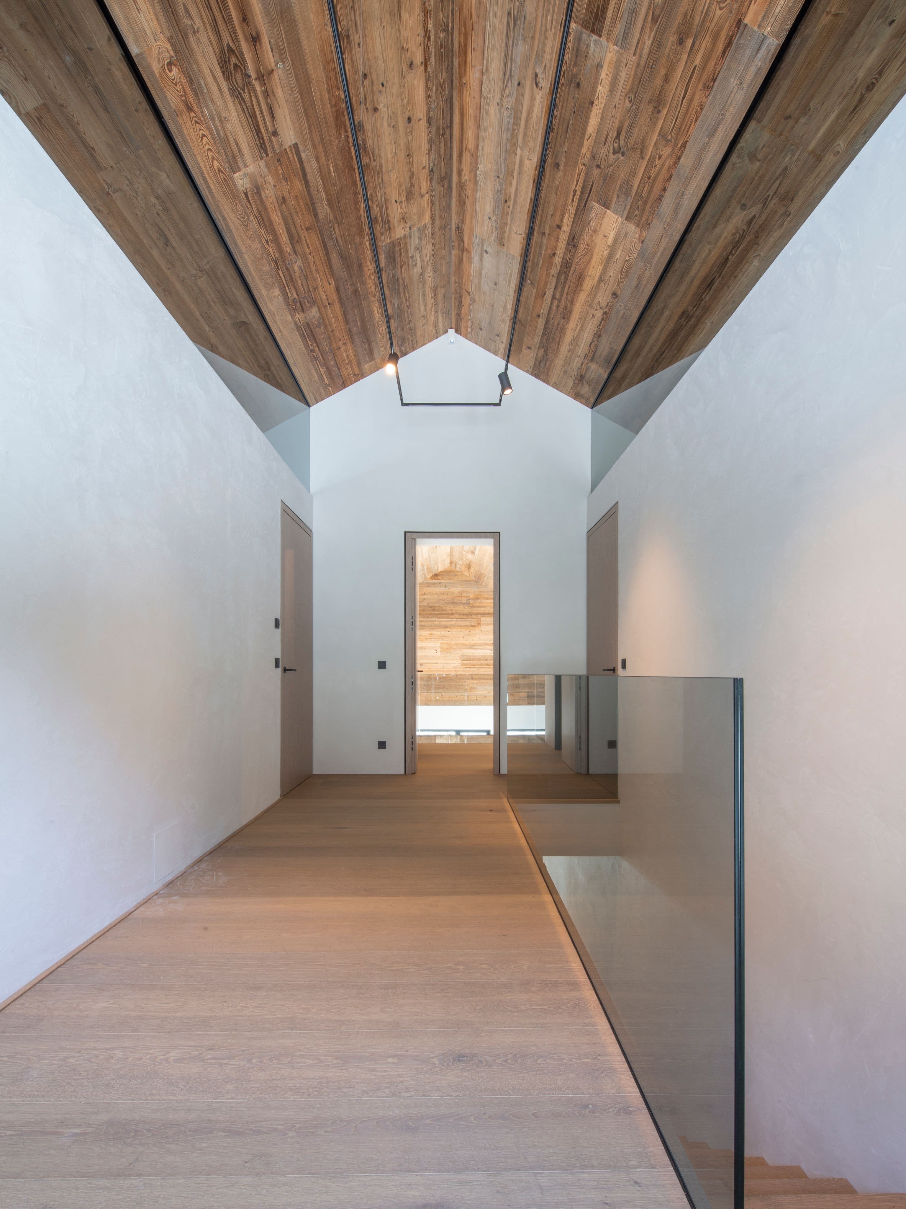 Flur im Obergeschoss mit Altholzdecke, Glasbrüstung und Blick auf die durchgängige Raumstruktur eines Privathauses in Tirol, Innenarchitektur Susanne Philippson