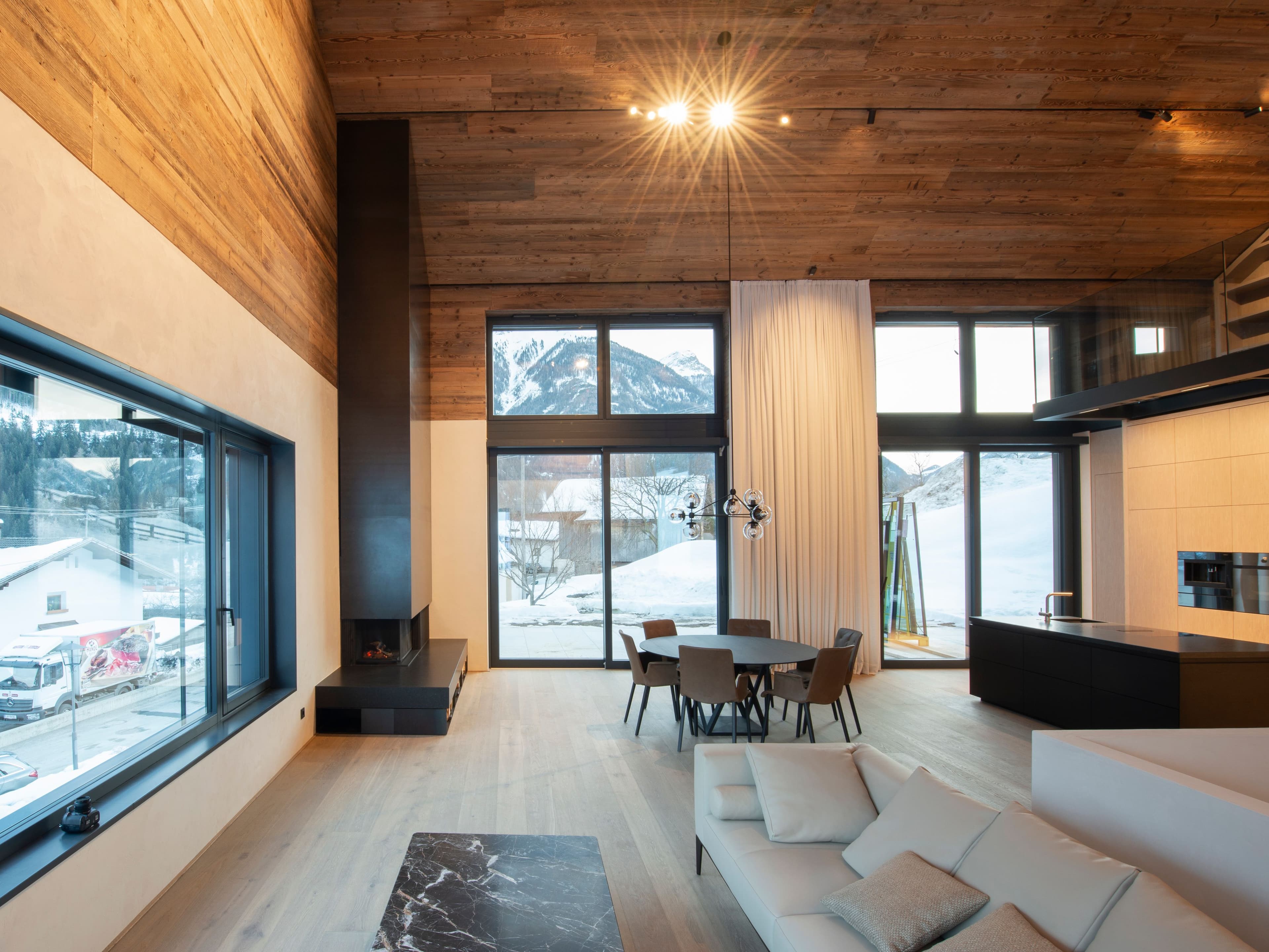 Offener Wohnraum über zwei Etagen mit Altholzdecke, Schwarzstahlkamin, Bergblick durch raumhohe Verglasung und einer Galerie mit maßgefertigtem Regal, Innenarchitektur Susanne Philippson