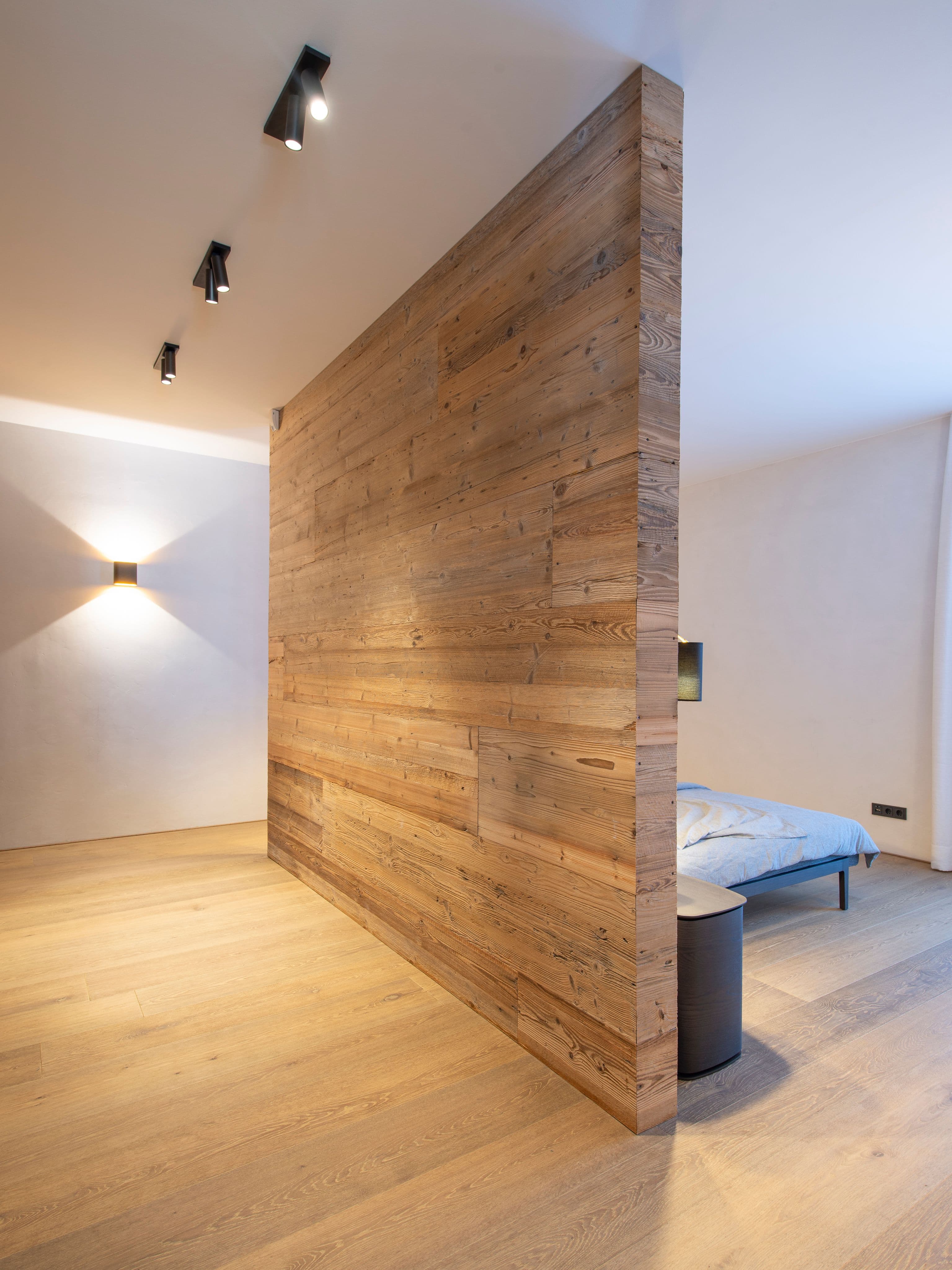 Schlafzimmer mit Altholzraumteiler, gepolstertem Bett und Wandleuchten sowie Gästezimmer mit freistehendem Altholzelement in einem Privathaus in Tirol, Innenarchitektur Susanne Philippson