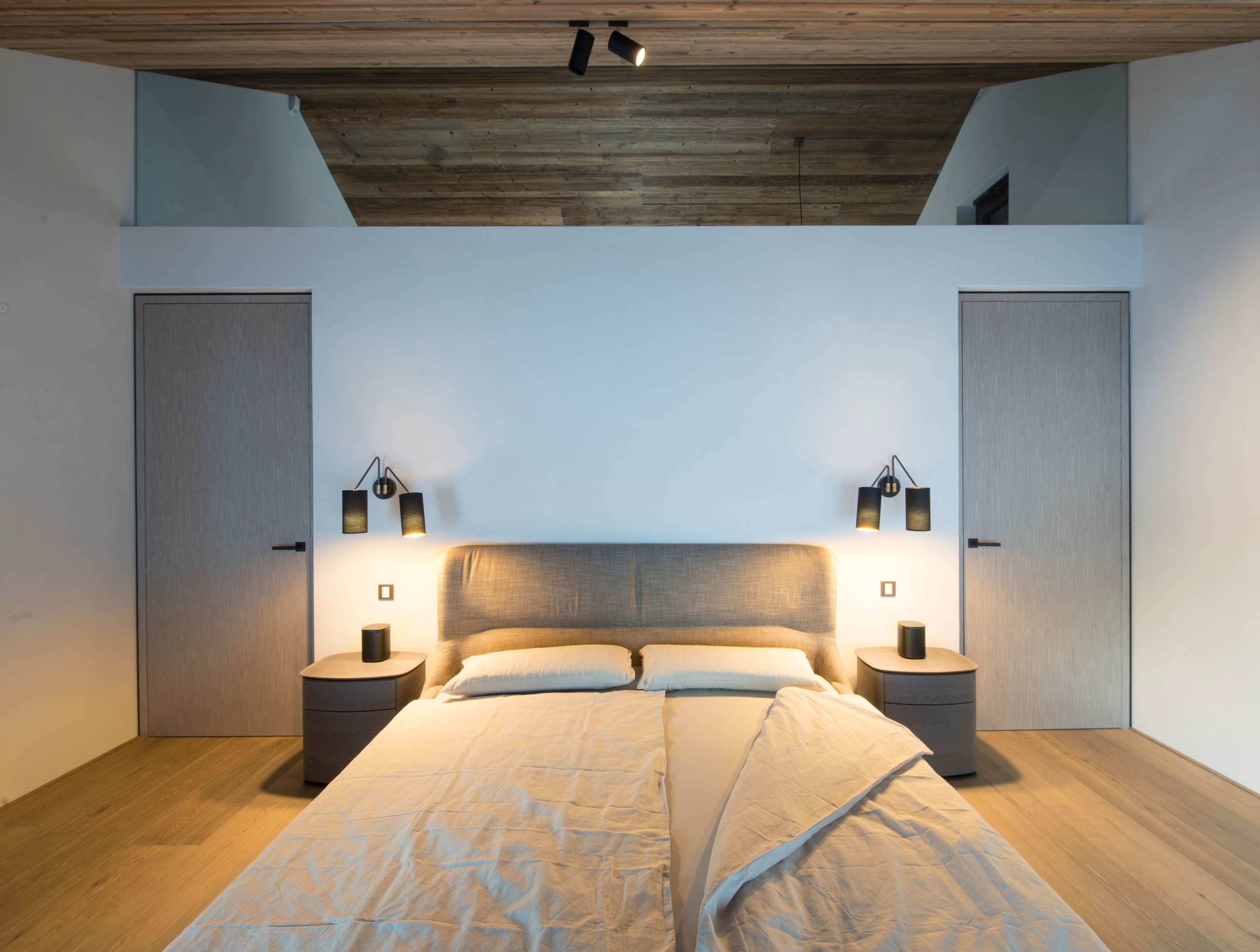 Schlafzimmer mit Altholzraumteiler, gepolstertem Bett und Wandleuchten sowie Gästezimmer mit freistehendem Altholzelement in einem Privathaus in Tirol, Innenarchitektur Susanne Philippson