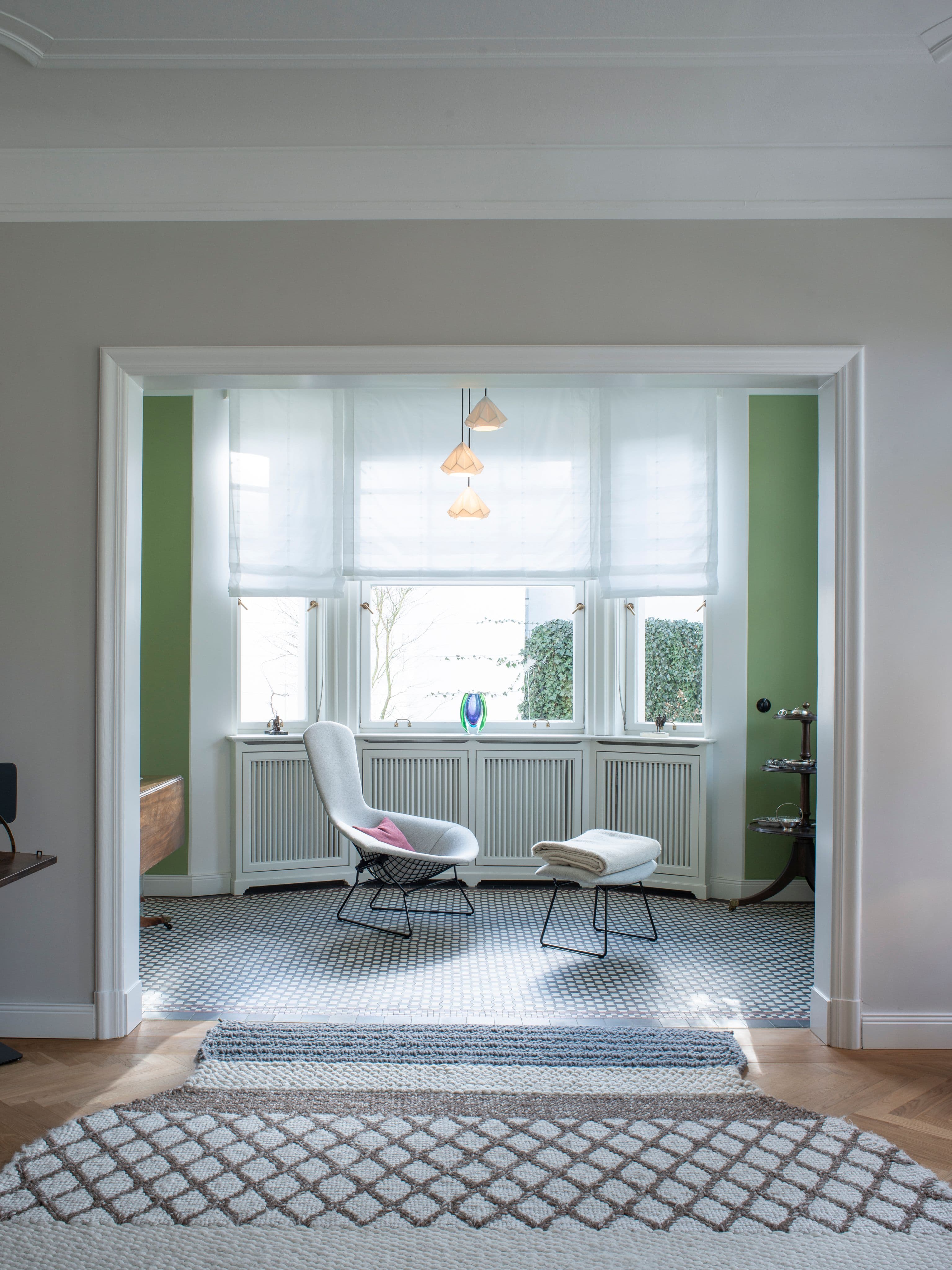 Wohnzimmer mit grauem Sofa und maßgefertigtem Regalschrank sowie Blick in das Lesezimmer mit Bertoia-Sessel und salbeigrünen Wänden in einem Privathaus, Innenarchitektur Susanne Philippson
