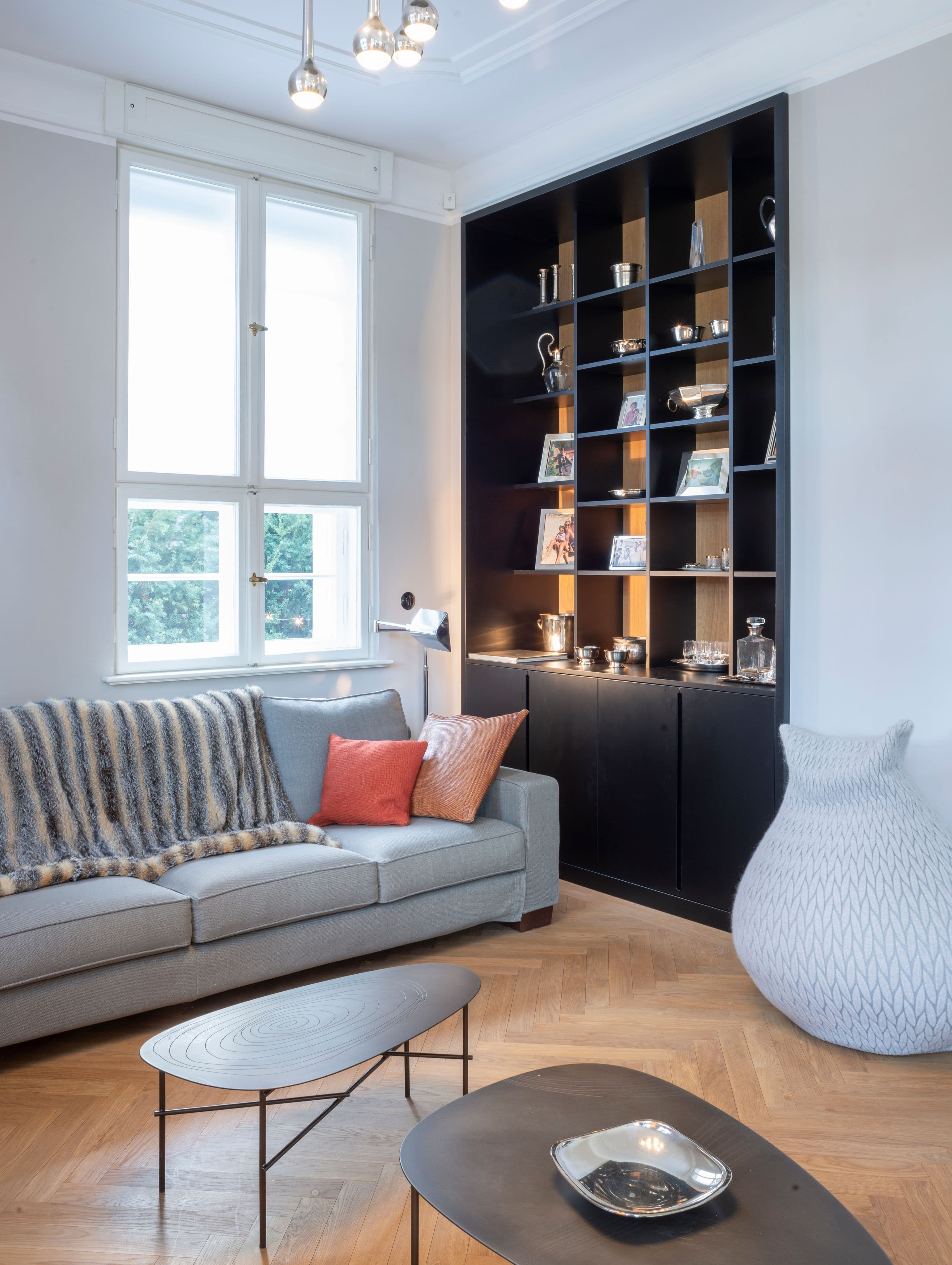 Wohnzimmer mit grauem Sofa und maßgefertigtem Regalschrank sowie Blick in das Lesezimmer mit Bertoia-Sessel und salbeigrünen Wänden in einem Privathaus, Innenarchitektur Susanne Philippson