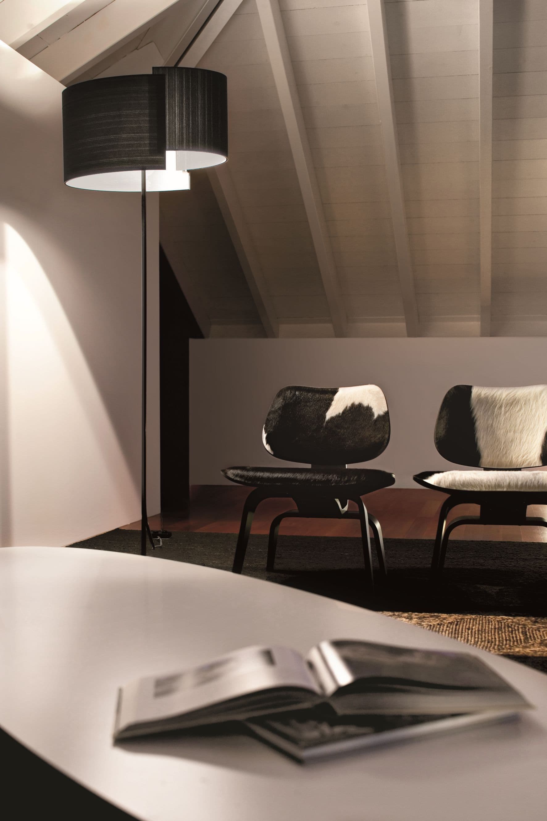 Joiin Stehleuchte von Pallucco in Schwarz mit kombinierten gebogenen Schirmflächen in Dachgeschossambiente mit Satteldachgebälk und Eames-Sesseln, Leuchtendesign Susanne Philippson