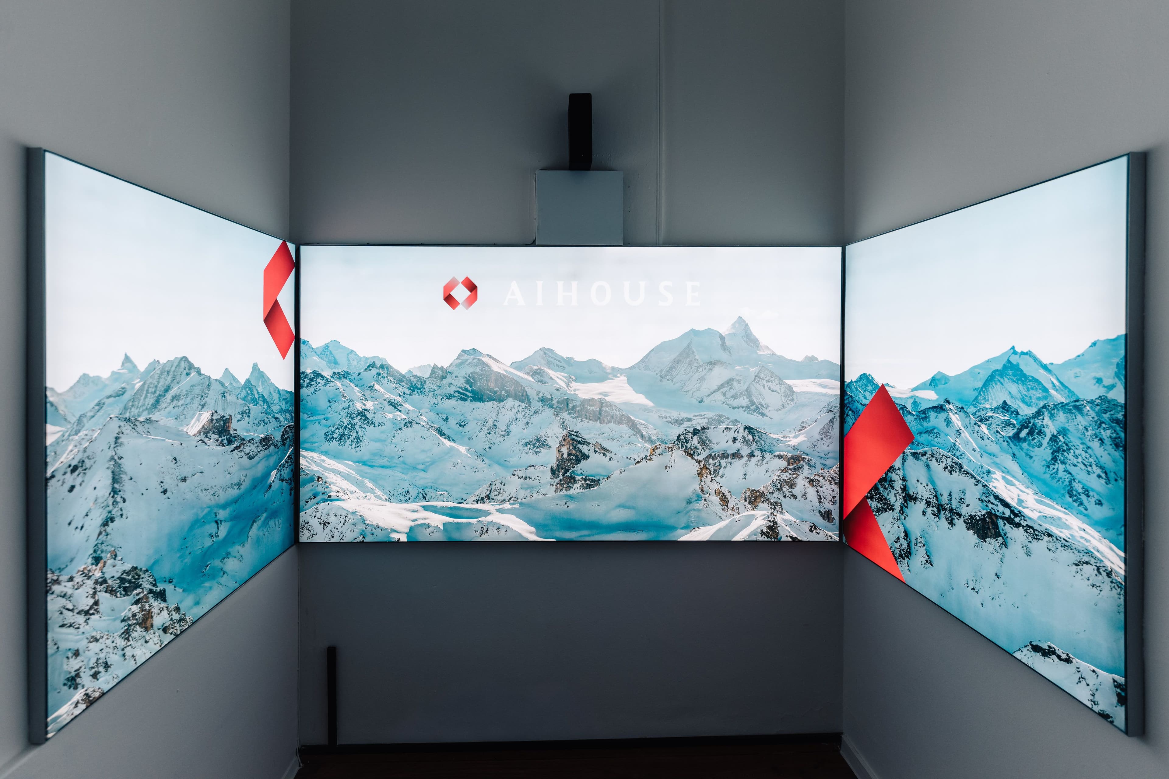 Dreiteiliges Display-Triptychon mit Alpenpanorama und AI House-Branding sowie dreidimensionalen roten Markenelementen an den Übergängen, Innenarchitektur Susanne Philippson