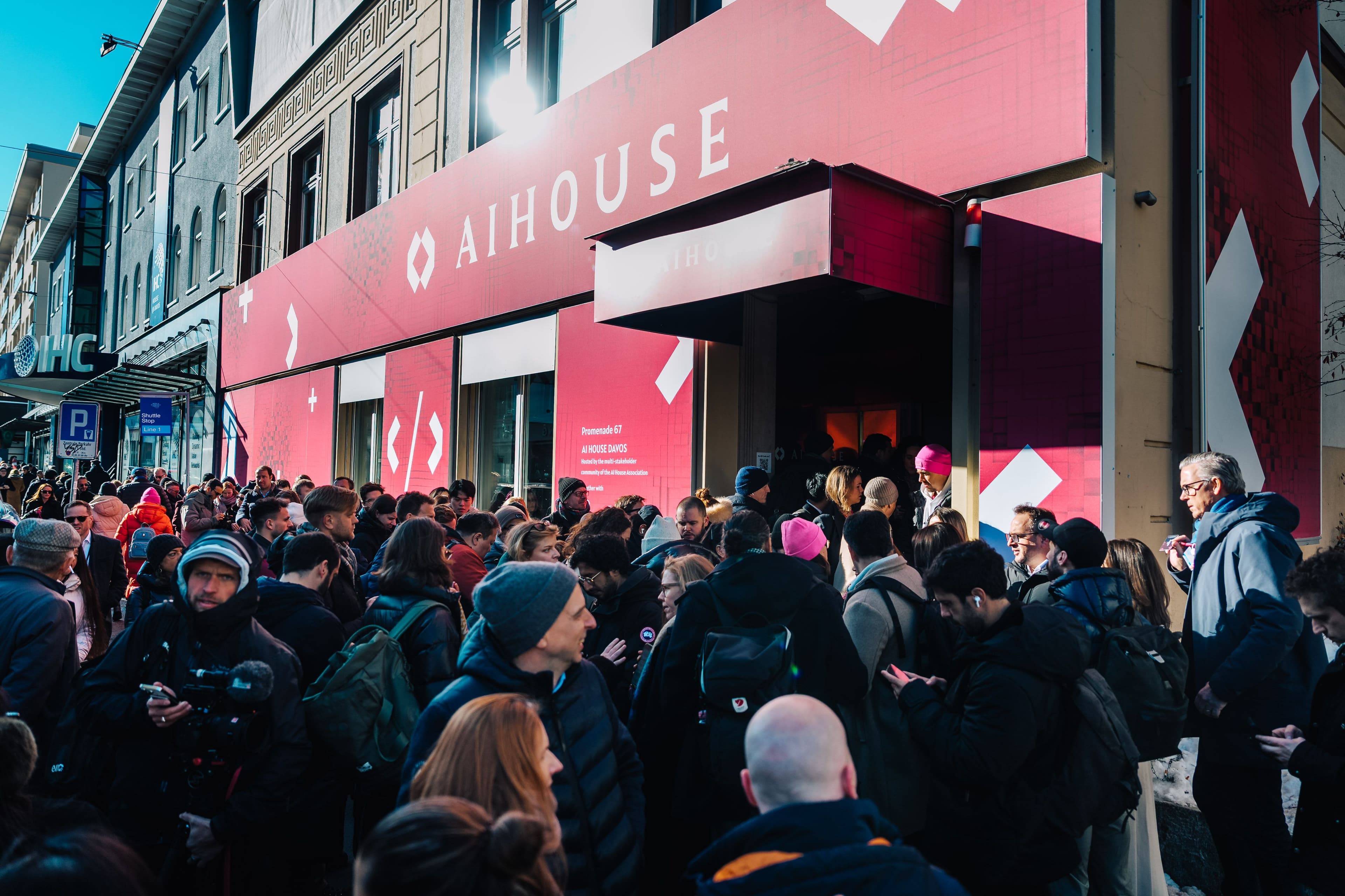 Außenansicht des AI House Davos an der Promenade mit großflächiger roter Markenbeschriftung und Menschenmenge vor dem Eingang, Innenarchitektur Susanne Philippson