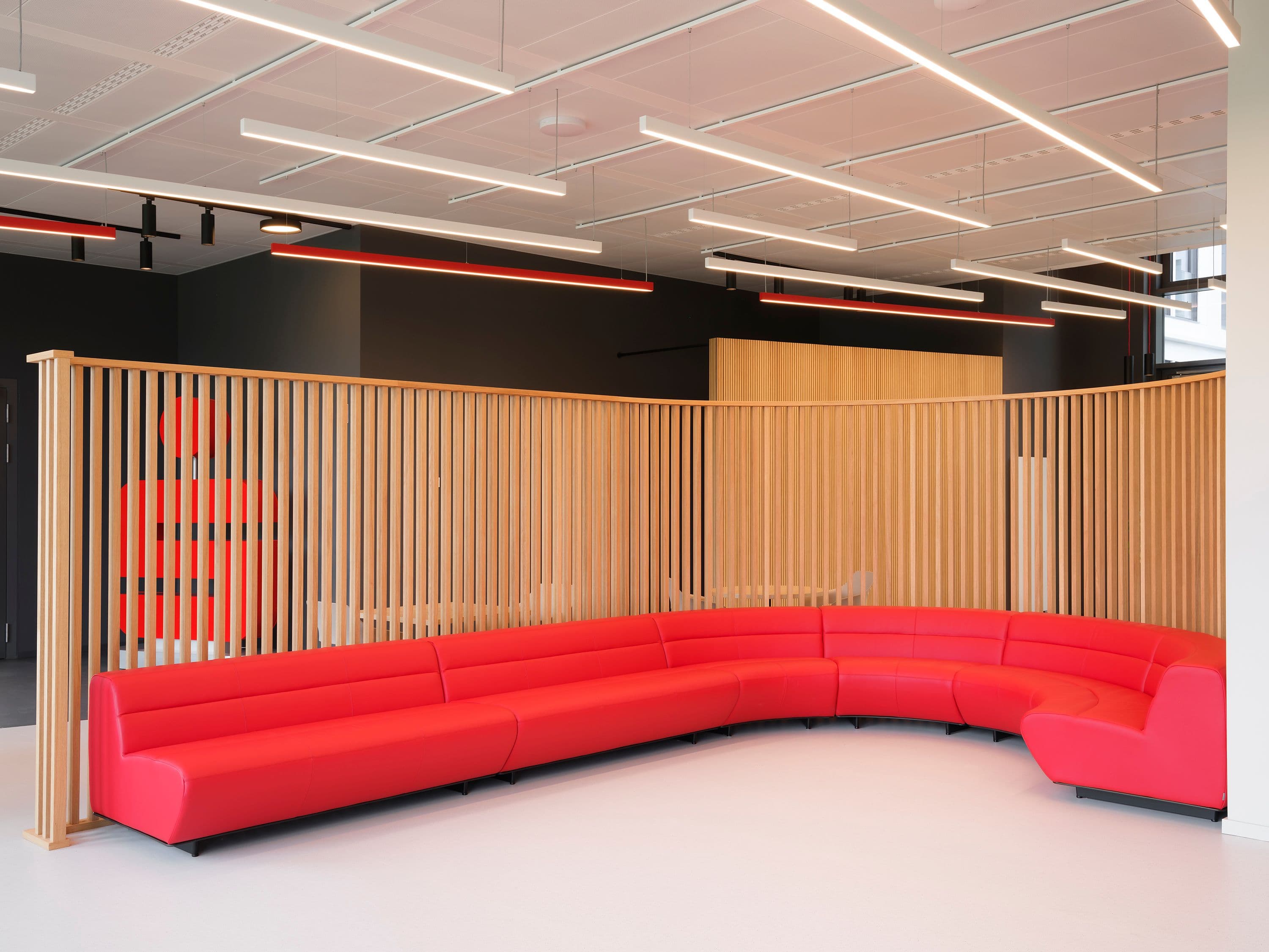 Kommunikationsbereich der Berliner Sparkasse mit geschwungenem roten Sofa, Holzlamellen und linearer Deckenbeleuchtung mit roten Akzentleuchten, Lichtplanung Susanne Philippson