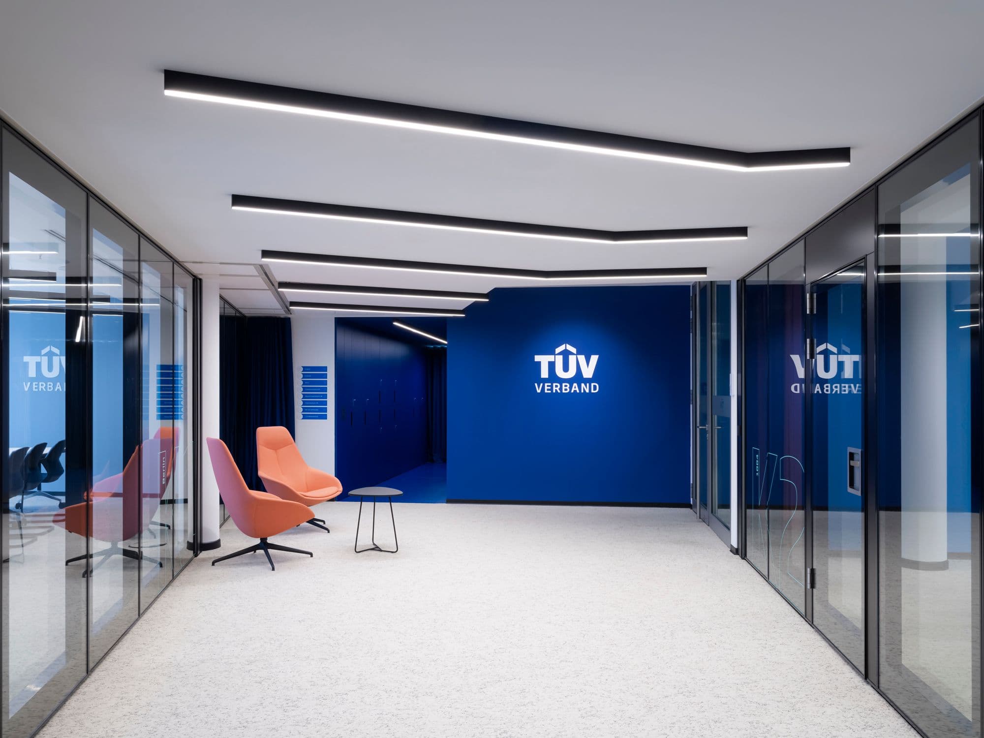 Empfangsbereich des TÜV Verband Berlin mit blauer Markenwand, Loungesessel von Wilkhahn und linearem Lichtkonzept an der Decke