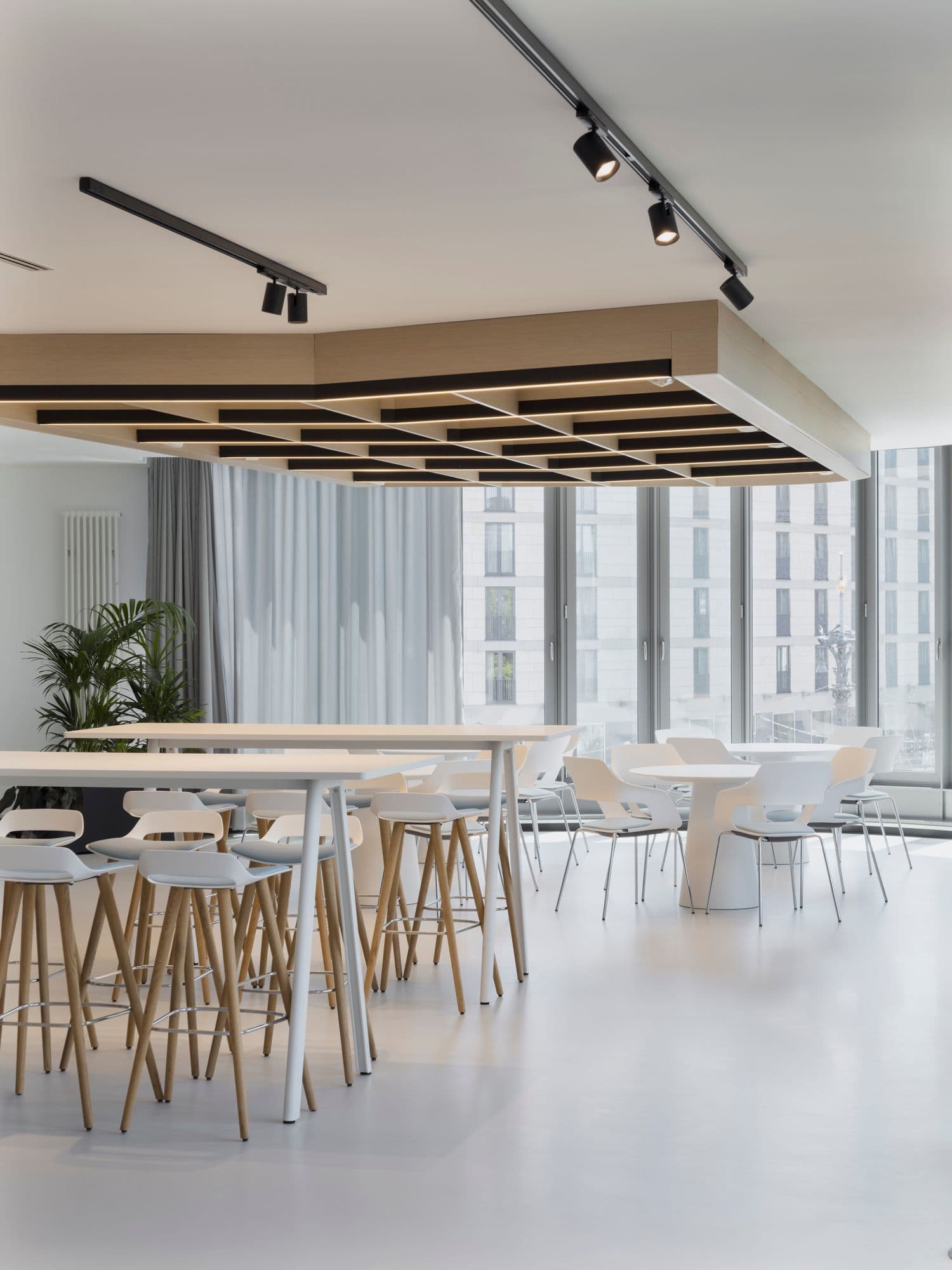 Heller Pausenbereich mit Stehtischen, Barhockern und Loungesessel von Wilkhahn sowie markanter Holz-Licht-Deckeninstallation im TÜV Verband Berlin