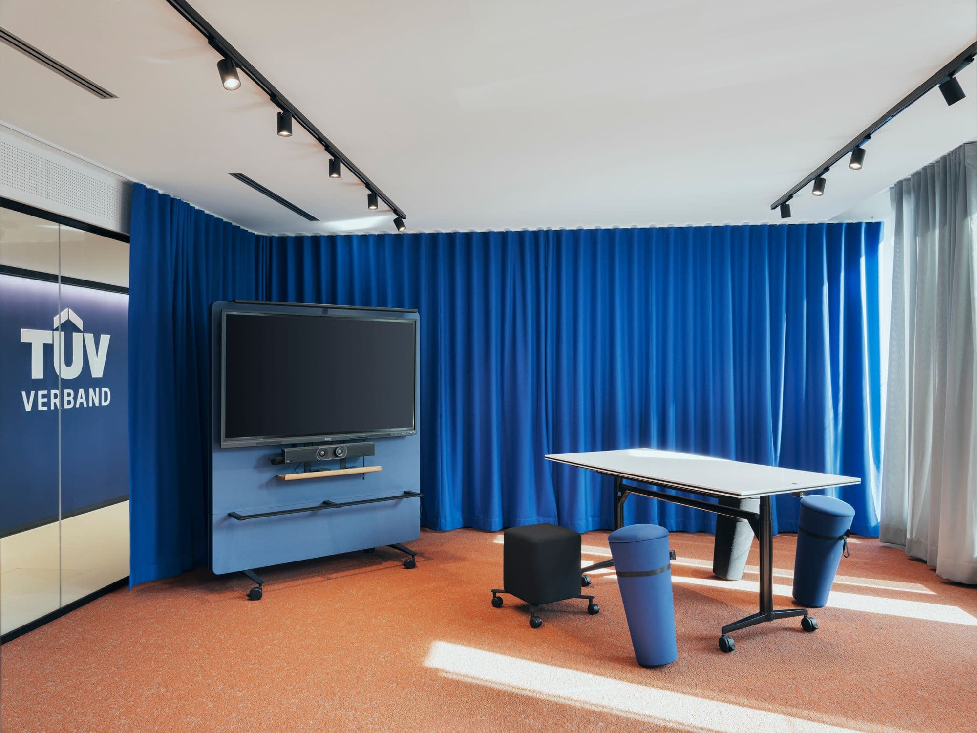 Flexibler Kreativraum mit blauem Akustikvorhang, mobilem Präsentationsbildschirm und zylindrischen Sitzelementen von Wilkhahn im TÜV Verband Berlin