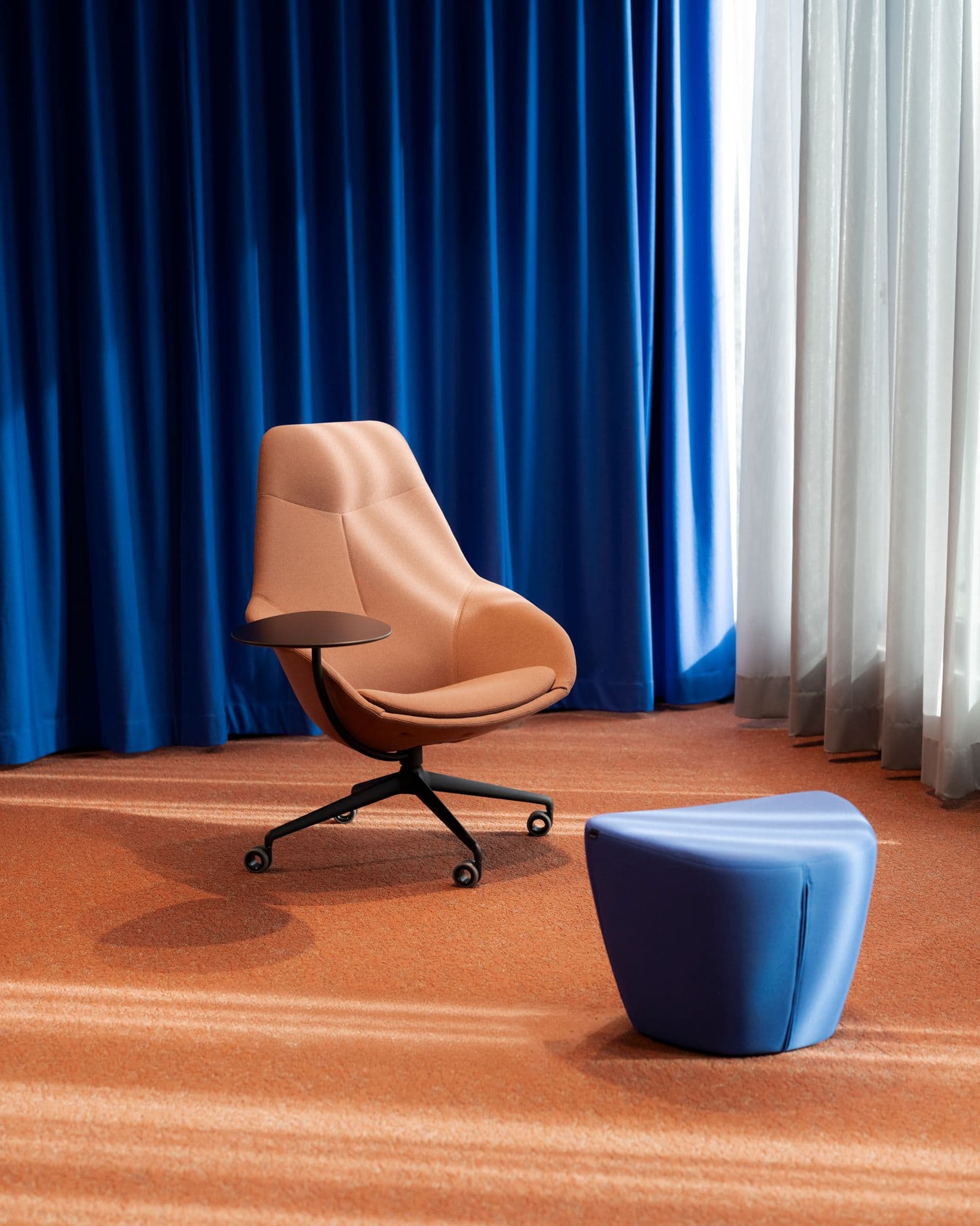 Detailaufnahme eines Wilkhahn-Loungesessel mit Beistelltablett und blauem Polsterhocker vor blauem Akustikvorhang im TÜV Verband Berlin